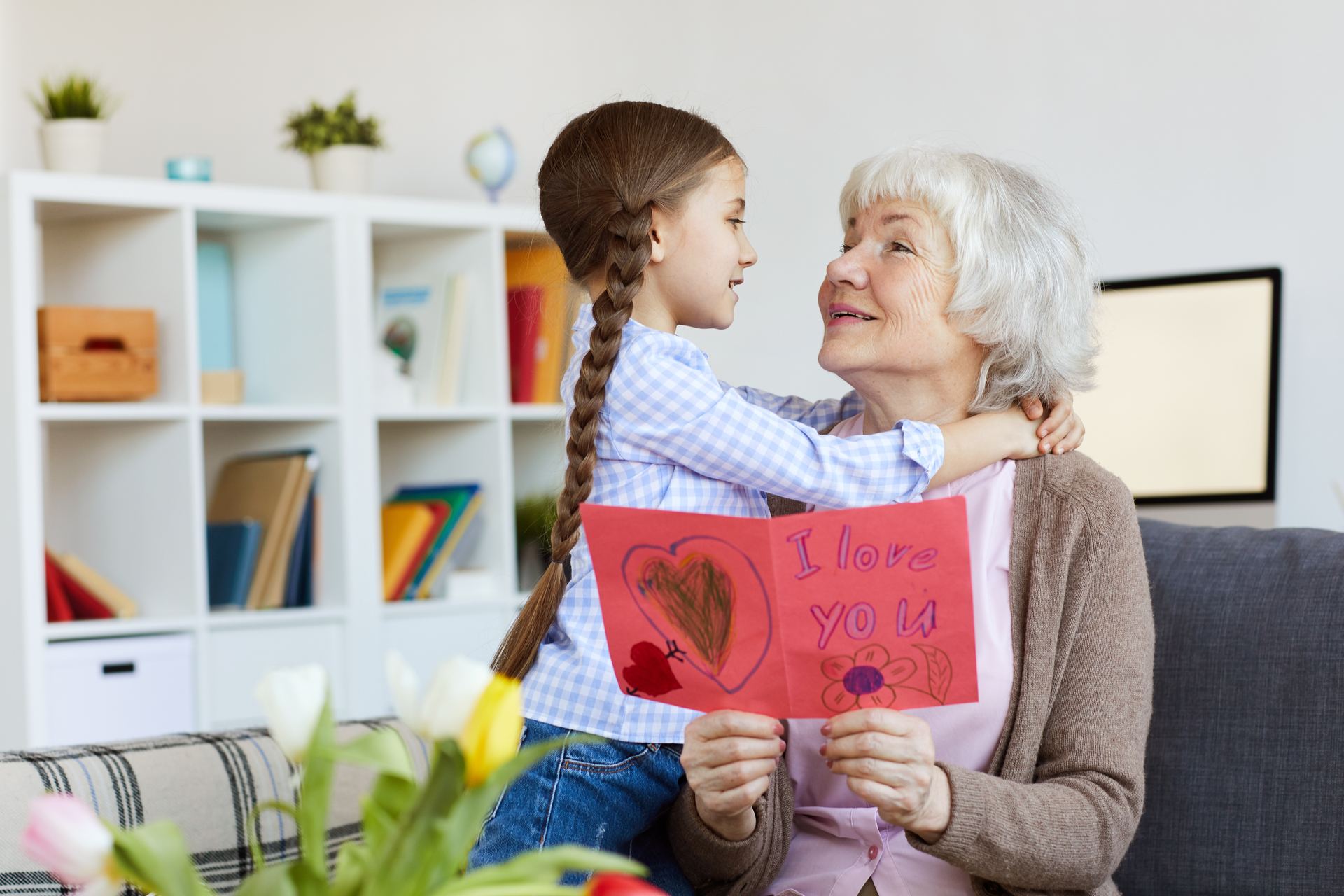 Grandmother smiling as her granddaughter hugs her and shares a handmade I love you card